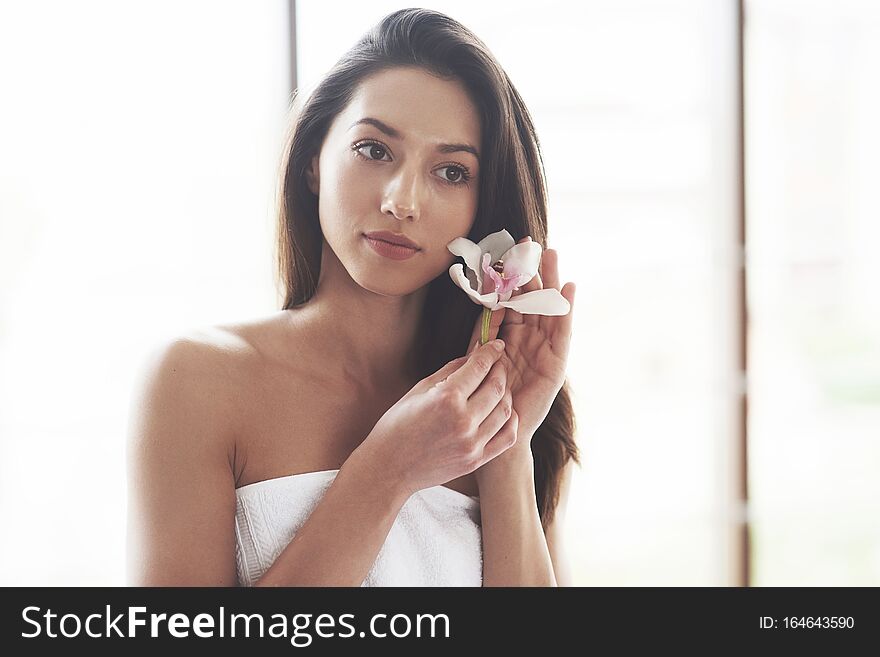 Beautiful young woman posing with orchid. Skin care treatment.