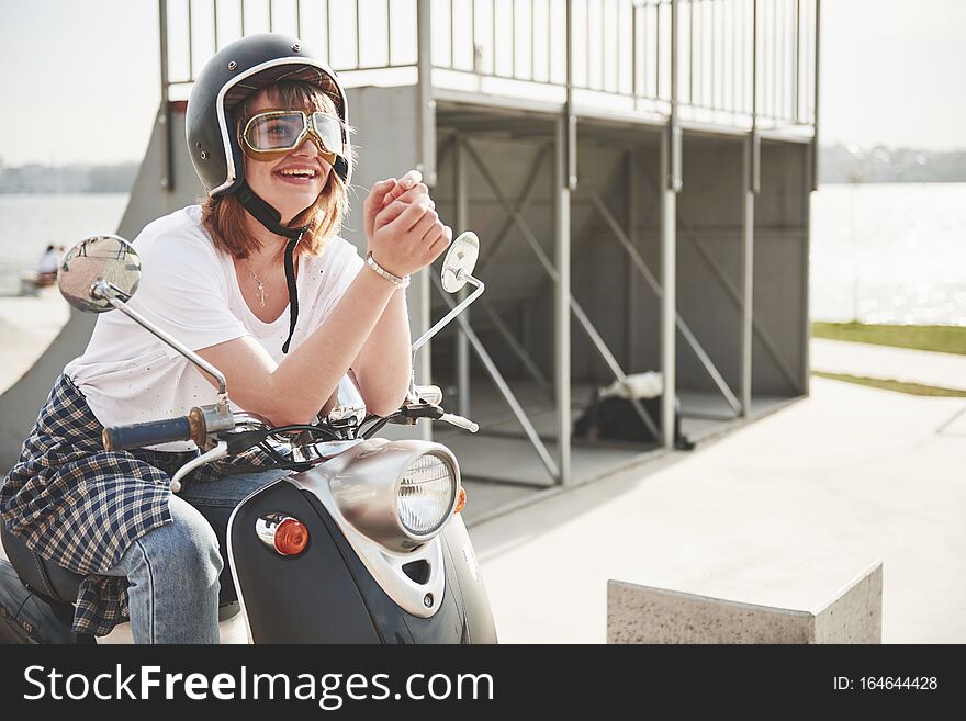 Portrait of a beautiful girl hipster sitting on a black retro scooter, smiling posing and enjoy the warm spring sunshine.