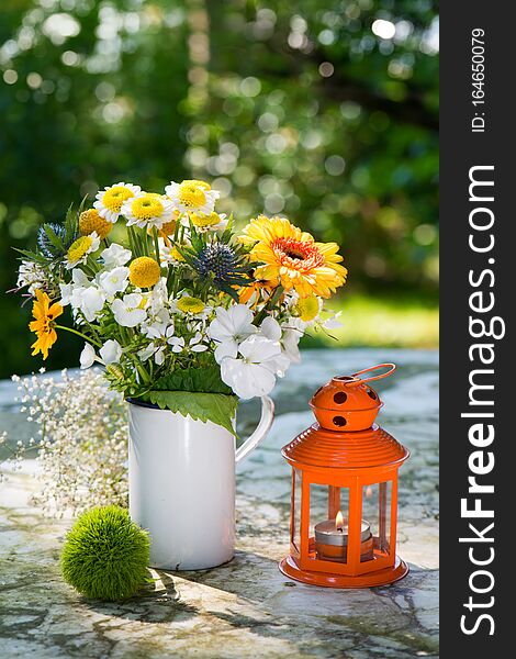 Summer flower bouquet with gerbera and eryngium in a old enamel cup on a garden table. Summer flower bouquet with gerbera and eryngium in a old enamel cup on a garden table