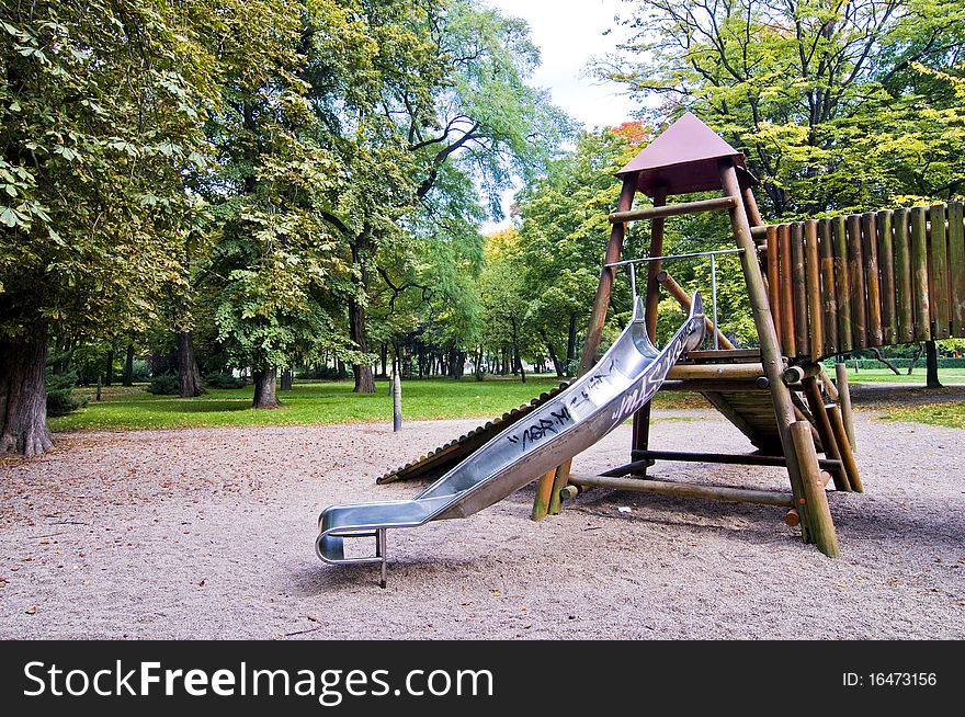 Slides in park during autumn, wide range of colors, green trees and yellow sand, wooden playground