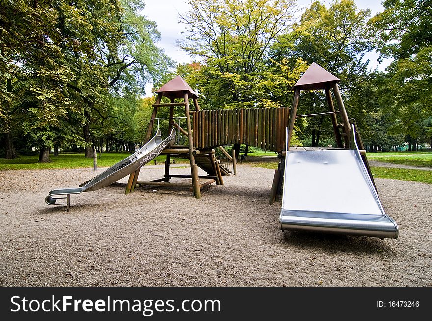 Slides in park during autumn, wide range of colors, green trees and yellow sand, wooden playground