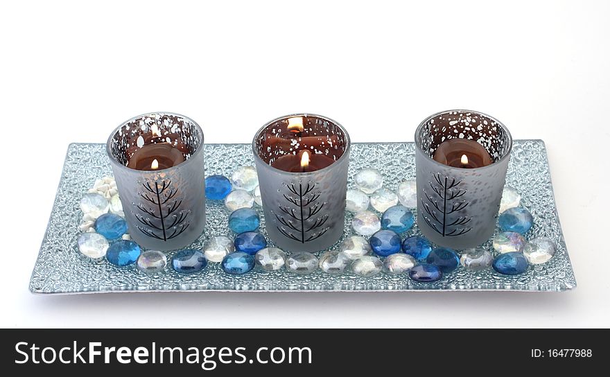 Three candles in decorative holders on a glass plate with coloured pebbles, over white. Christmas theme. Three candles in decorative holders on a glass plate with coloured pebbles, over white. Christmas theme.