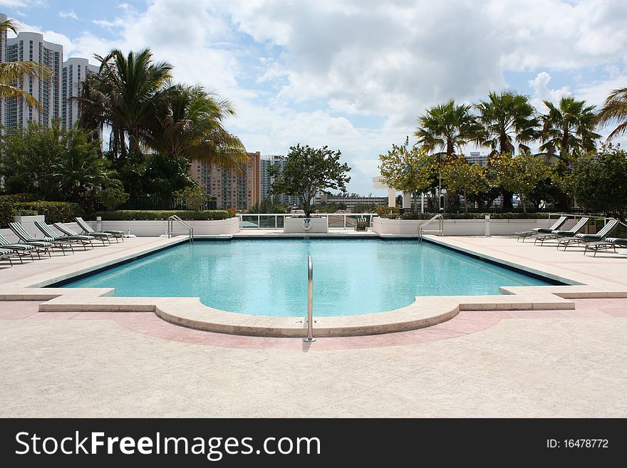 A swimming pool in the tropics surrounded by palm trees and sunshine.