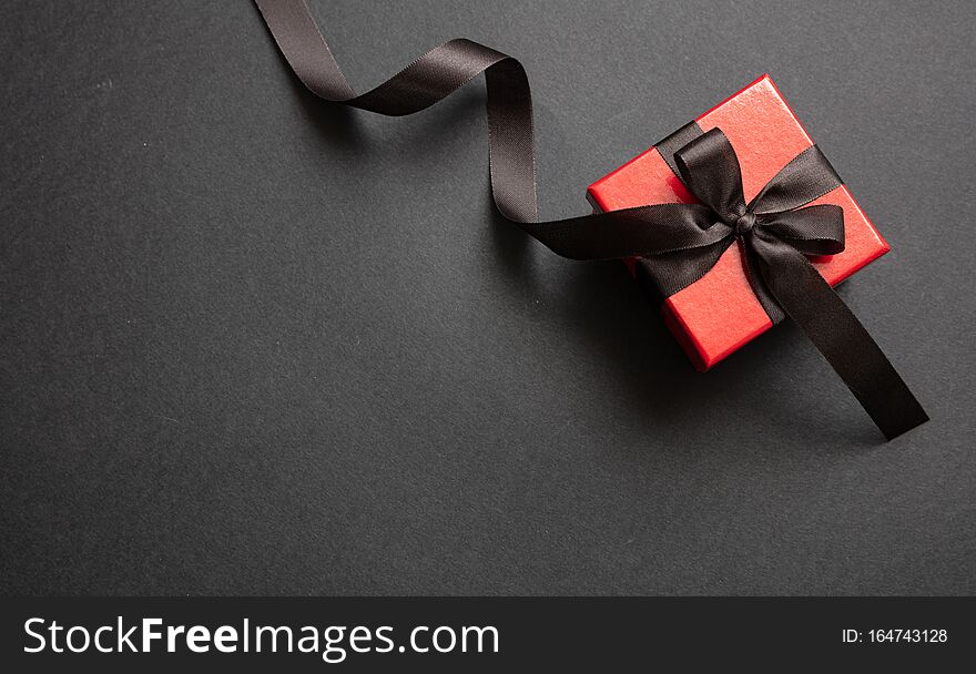 Black Friday sale concept. Red color gift box with black ribbon isolated against black background, top view. Black Friday sale concept. Red color gift box with black ribbon isolated against black background, top view