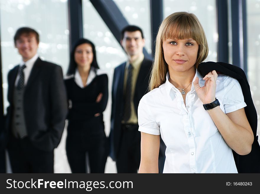 A young blond businesswoman in formal clothes in front of her colleagues. The image is taken on an abstract background. A young blond businesswoman in formal clothes in front of her colleagues. The image is taken on an abstract background.