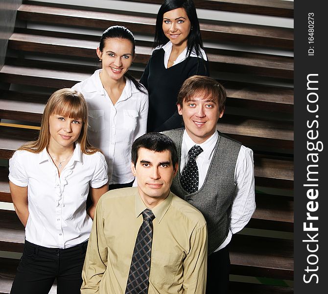 A group of five young and happy businesspersons in formal clothes. The image is taken on a staircase. A group of five young and happy businesspersons in formal clothes. The image is taken on a staircase.