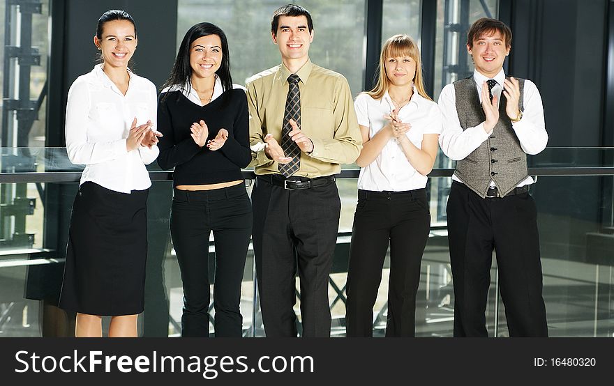 Five young businesspersons in formal clothes are clapping their hands. The image is taken on an office background. Five young businesspersons in formal clothes are clapping their hands. The image is taken on an office background.