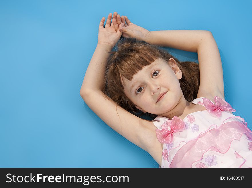 The little girl lies relax on a blue background. Empty space. The little girl lies relax on a blue background. Empty space.