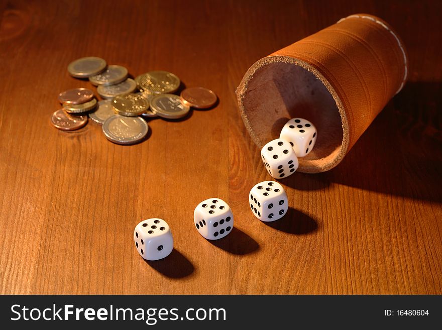 Five white dice and leather cup near coins lying on wooden background. Five white dice and leather cup near coins lying on wooden background