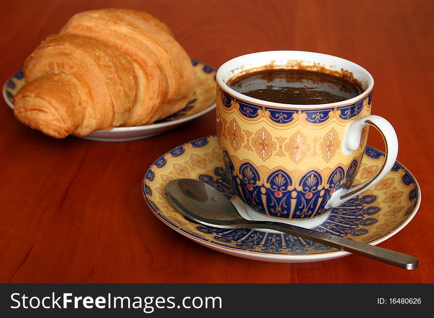 A cup of coffee with croissant. Shallow depth of field. Focus on the cup. A cup of coffee with croissant. Shallow depth of field. Focus on the cup.