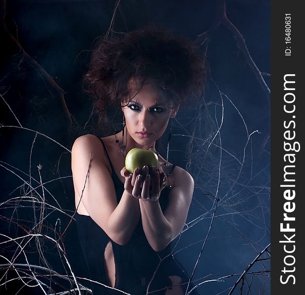 Fashion shoot of a young and attractive girl in a bizarre dress with a green apple. The image is taken on a mystique background with branches. Fashion shoot of a young and attractive girl in a bizarre dress with a green apple. The image is taken on a mystique background with branches.