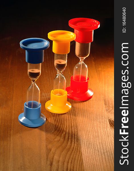 Three colored hourglasses standing on wooden background. Three colored hourglasses standing on wooden background