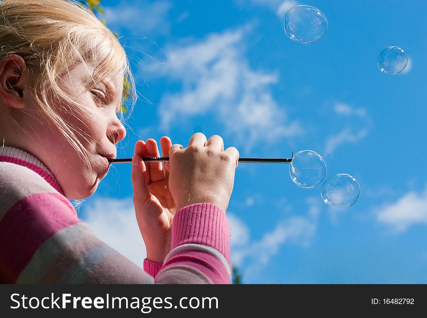 Girl starting up soap bubbles against blue sky
