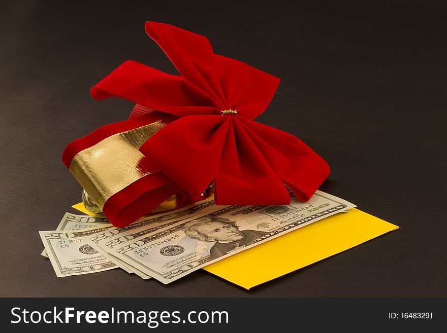 Sunny yellow envelope with a gift of cash in American currency is in a yellow envelope with red velvet bow accent against a black background to show the holiday gift of choice, especially in a recession and during hard times;. Sunny yellow envelope with a gift of cash in American currency is in a yellow envelope with red velvet bow accent against a black background to show the holiday gift of choice, especially in a recession and during hard times;