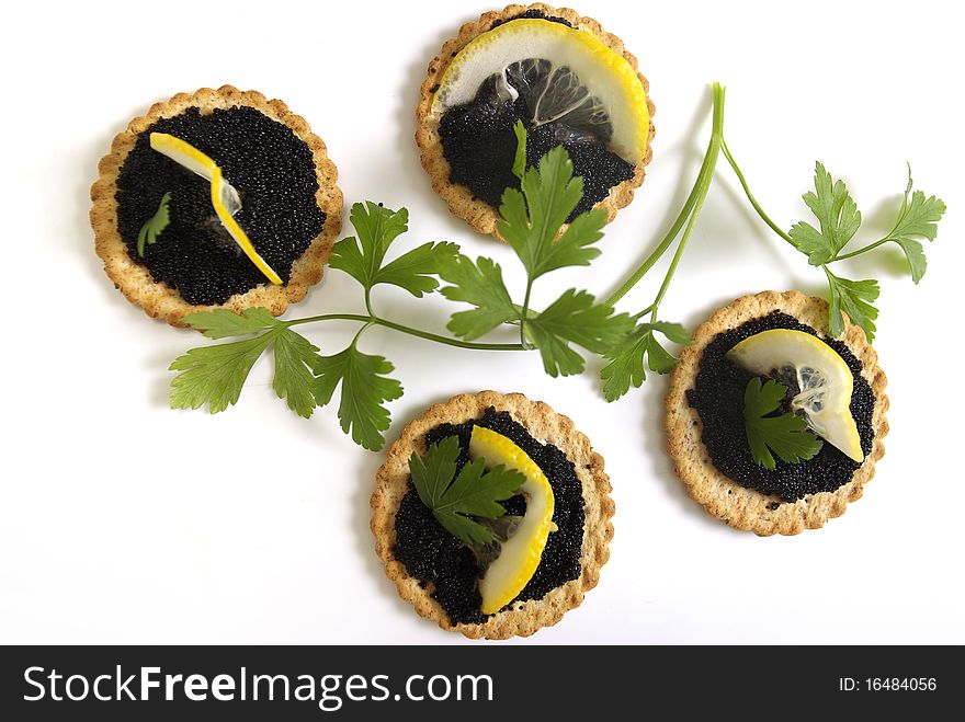 Caviar appetizers on biscuit, served with a slice of lemon and decorated with parsley