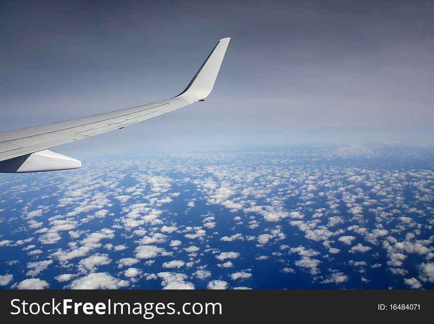 Plane wing in the sky with small clouds below and approaching darkness. Plane wing in the sky with small clouds below and approaching darkness