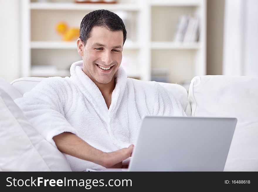 Laughing young man in a bathrobe looking at laptop. Laughing young man in a bathrobe looking at laptop