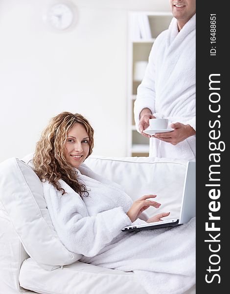 A man in a robe brings coffee girl with laptop. A man in a robe brings coffee girl with laptop