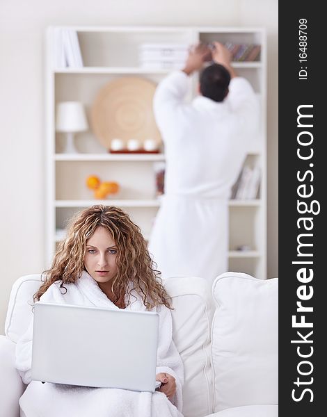 A girl in a bathrobe looking at a laptop in the foreground. A girl in a bathrobe looking at a laptop in the foreground