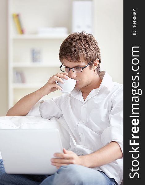 A young man with a cup of looking at the laptop at home. A young man with a cup of looking at the laptop at home