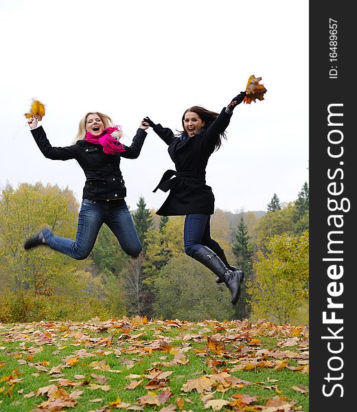 Two autumn girl friends in a park jumping