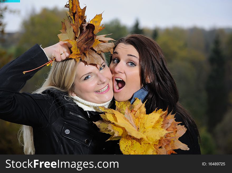 Two beautiful girl friends with autumn leafs in a park looking up