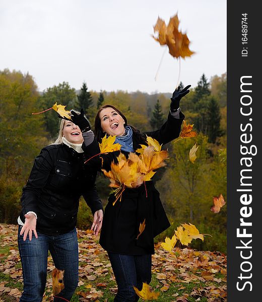 Two beautiful girl friends with autumn leafs in a park looking up