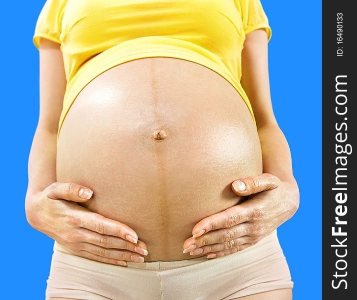 Closeup stomach and hands of pregnant woman on blue background