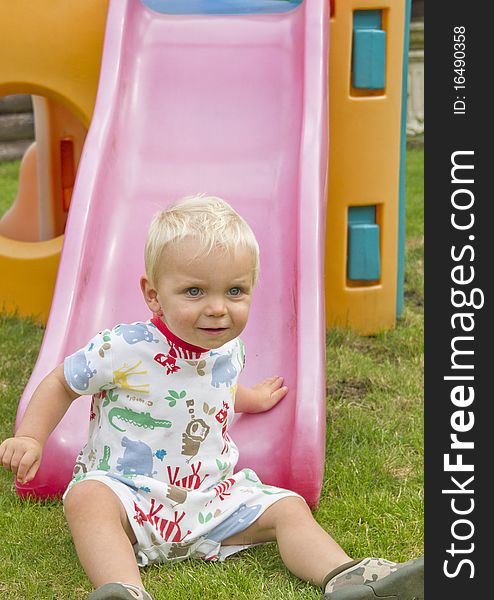 Cute blond toddler at the bottom of a slide. Cute blond toddler at the bottom of a slide