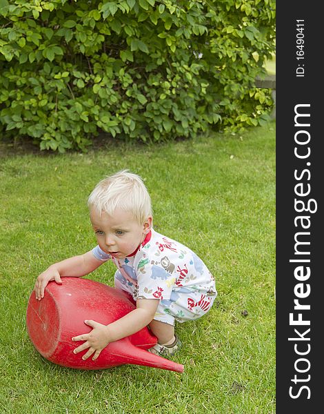 Cute blond toddler trying to pick up a red watering can. Cute blond toddler trying to pick up a red watering can