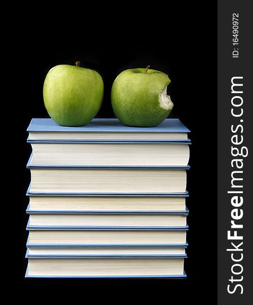 Green apples on a stack of books isolated on black