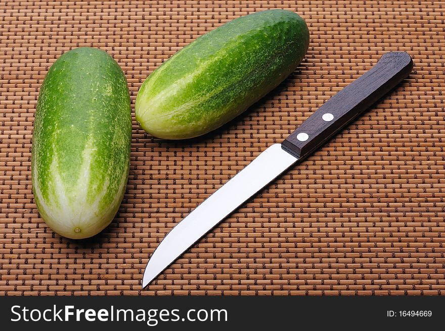 Two cucumbers and knife lie on brown braided mat