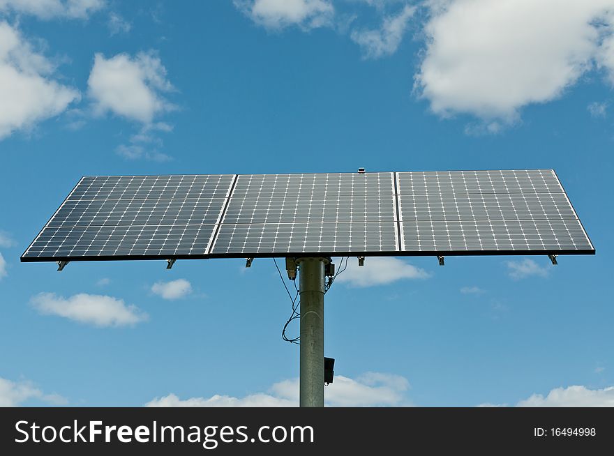 A modern photovoltaic solar panel array generates electricity with blue sky and clouds in the background. A modern photovoltaic solar panel array generates electricity with blue sky and clouds in the background.