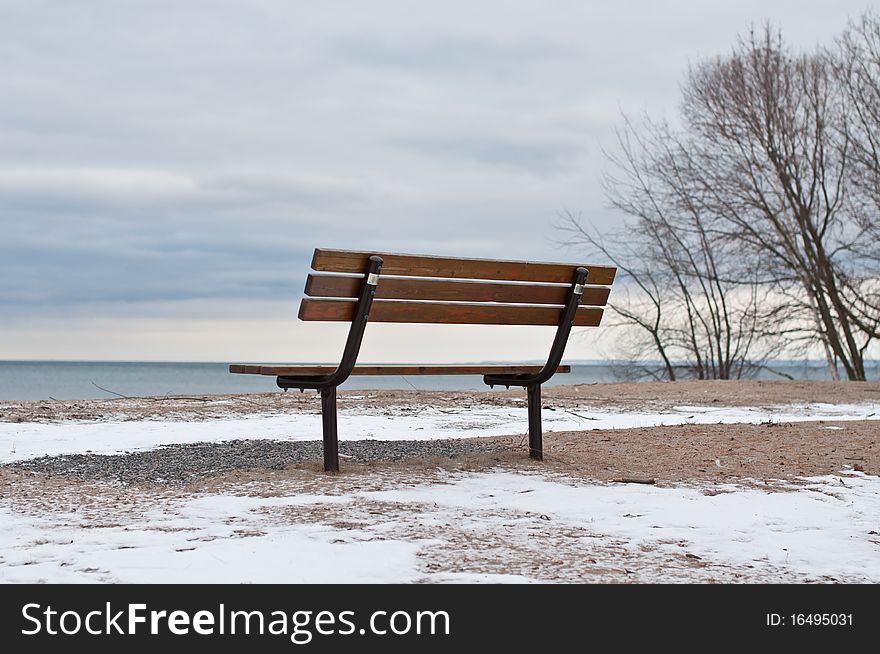 A park bench sits empty by the shore of a lake in winter. A park bench sits empty by the shore of a lake in winter.
