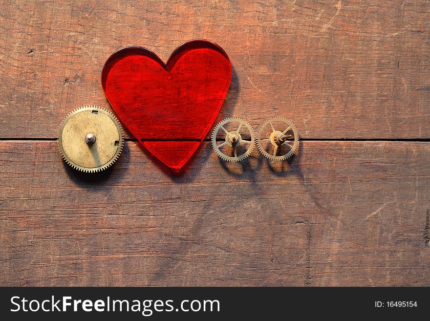 Red glass heart and gears on wooden background. Red glass heart and gears on wooden background