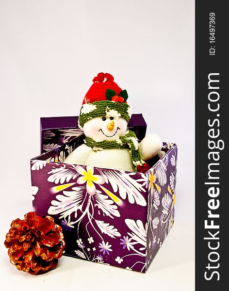 A toy snowman popping out of a purple gift box and a pine cone next to it. A toy snowman popping out of a purple gift box and a pine cone next to it