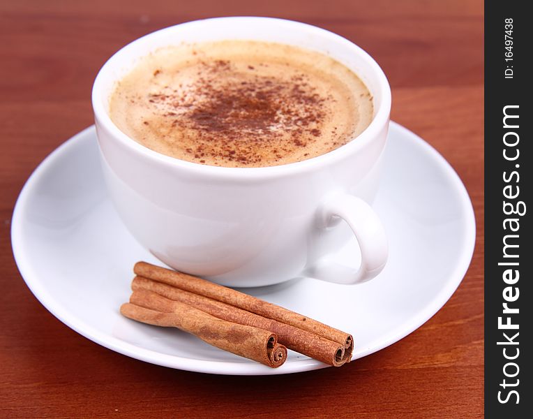 Cup of coffee sprinkled with cinnamon and with cinnamon sticks on wooden background