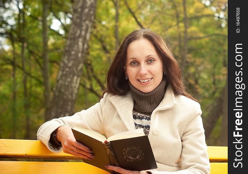 Young smilling woman sitting on bench with book. Young smilling woman sitting on bench with book