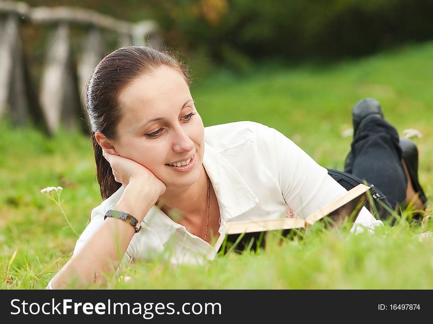 Young woman reading book on green field