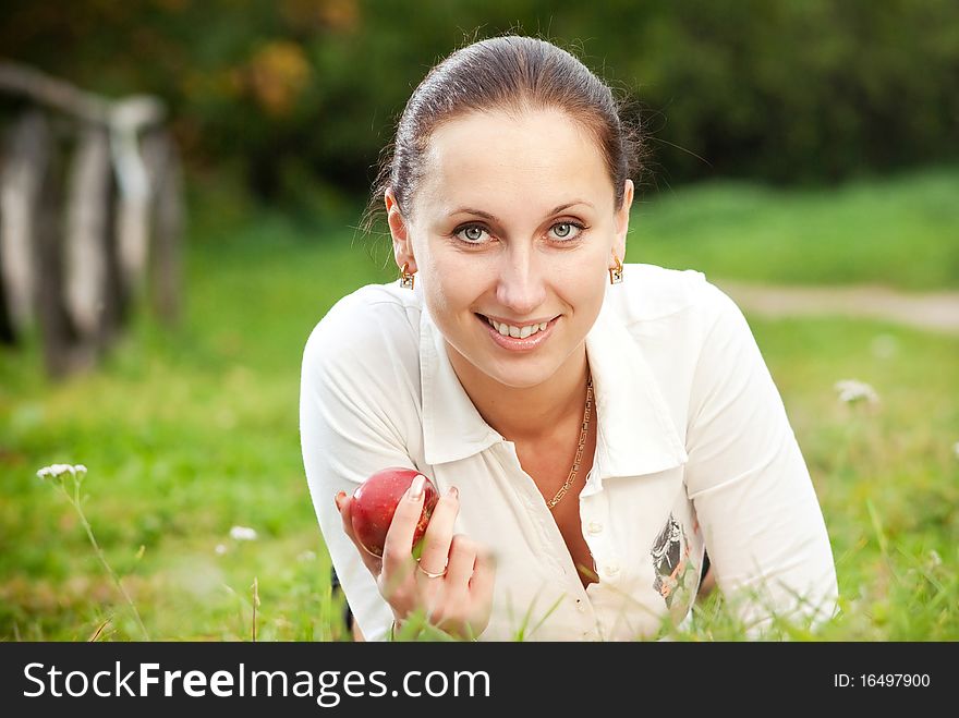 Young woman smilling with apple on grass