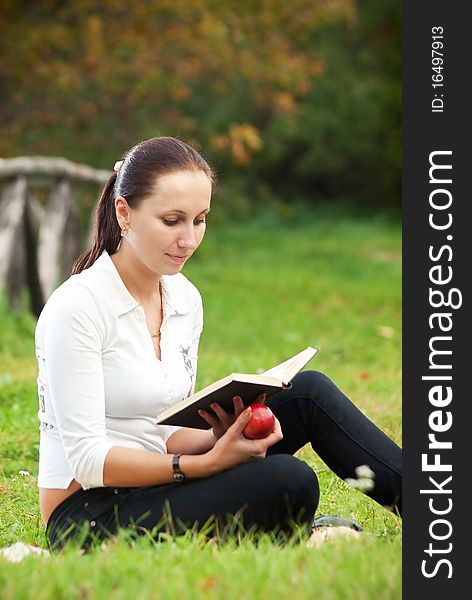 Young Woman Sitting On Grass And Reading Book