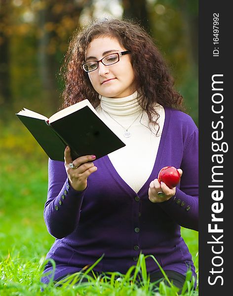 Woman reads book on green grass with red apple in hand