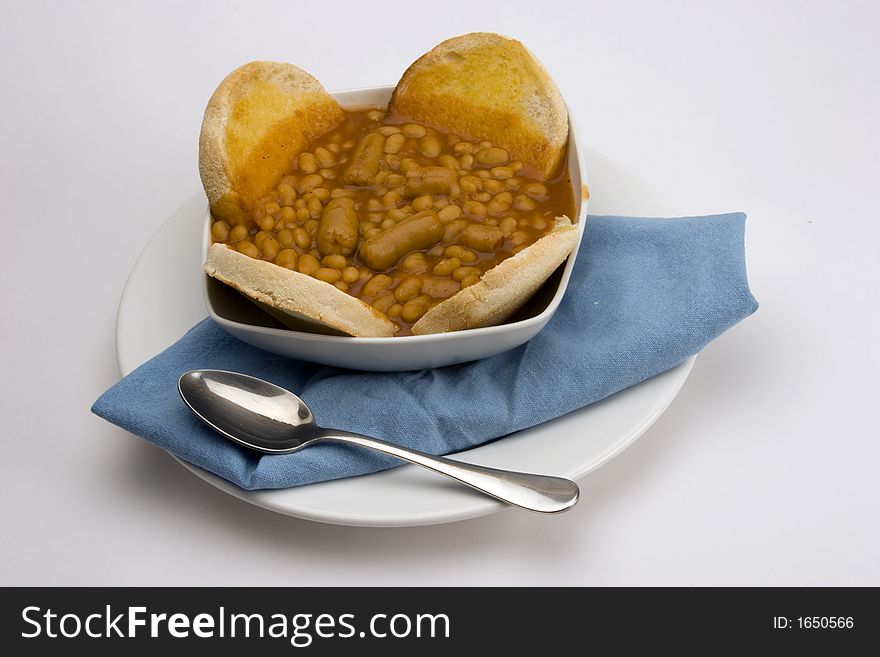Baked beans with English muffin in a Bowl with Blue Cloth and spoon.