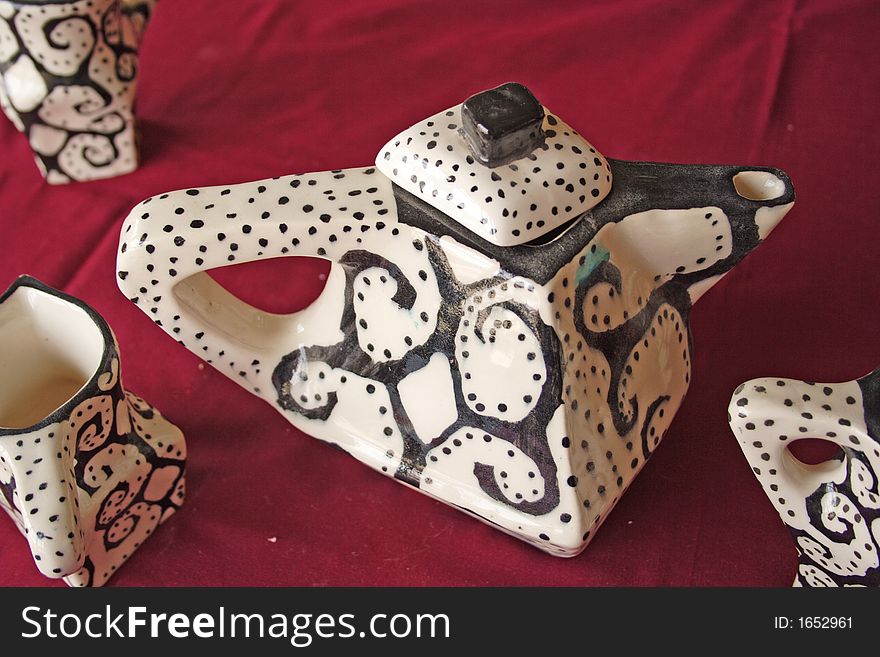 This unusual teapot was exhibited at a centre for the development of young African artists.The teapot has unusually sharp edges, repeated by the dark ethnic pattern painted on it. This unusual teapot was exhibited at a centre for the development of young African artists.The teapot has unusually sharp edges, repeated by the dark ethnic pattern painted on it.