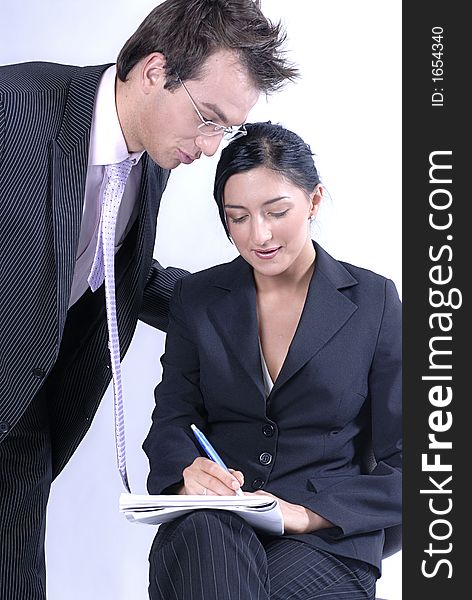 Picture of standing standing man business reading notes and woman sitting on chair and holding notes and pen, both business dressed. Picture of standing standing man business reading notes and woman sitting on chair and holding notes and pen, both business dressed.