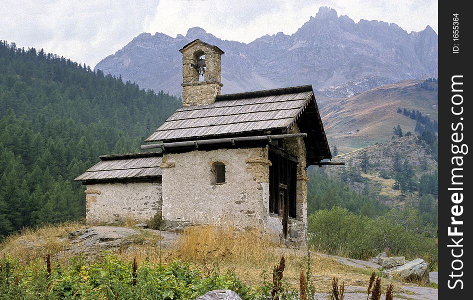 Very little mountain chapel on wood and rocks background in southern french Alps