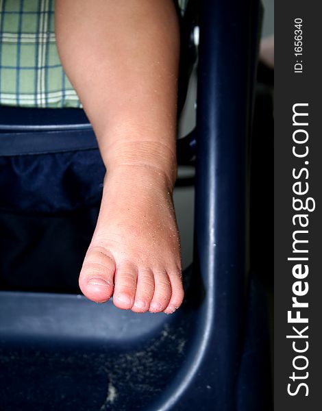 Foot and leg of a toddler girl sitting in a stroller with some fine sand on the skin. Foot and leg of a toddler girl sitting in a stroller with some fine sand on the skin