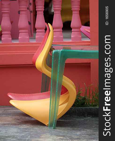 Two plastic chairs, red and orange, leaningh against transparent, green table on a red and pink background. Two plastic chairs, red and orange, leaningh against transparent, green table on a red and pink background.