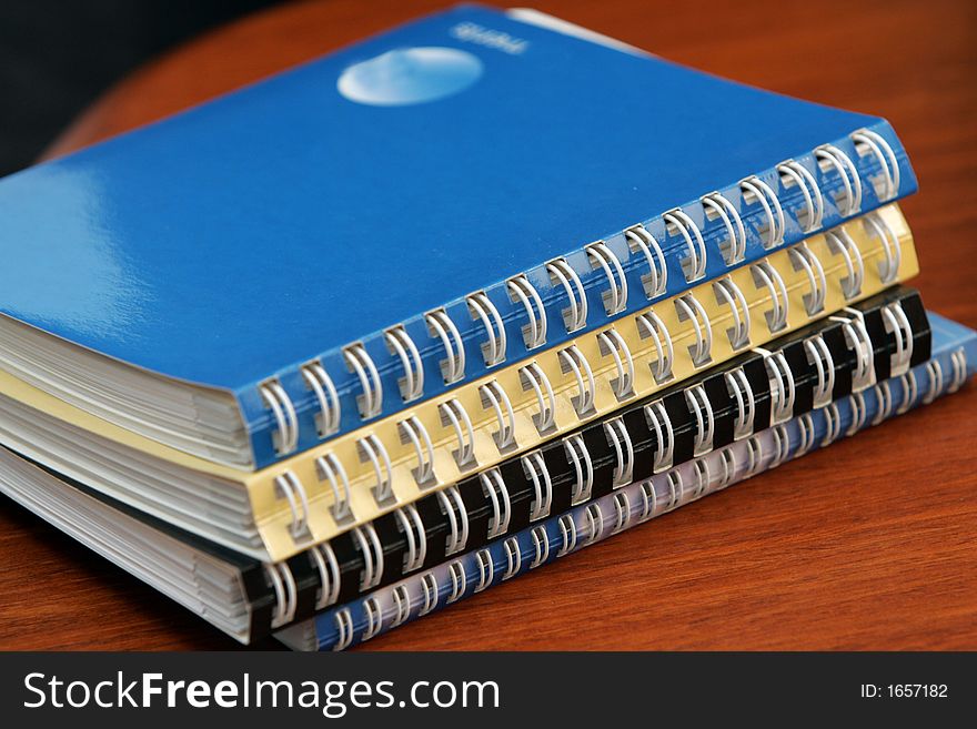 A pile of diaries lying on a wooden office desk. A pile of diaries lying on a wooden office desk