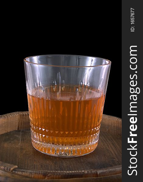 Glass of whiskey standing on a old wooden barrel, everything on a black background. Glass of whiskey standing on a old wooden barrel, everything on a black background